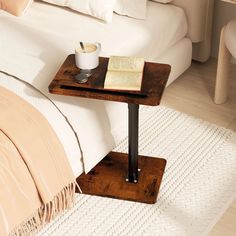 a small wooden table with a book and cup of coffee on it next to a bed