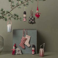 christmas stockings and ornaments hanging from a tree in front of a gray wall with pine branches