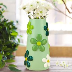 a green vase filled with white flowers on top of a wooden table