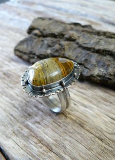 Made with a 18x24 mm natural, painted jasper cabochon, this ring reminds me of Western fields and open roads. The sandy colored gem sits on a 25x34mm base that is adorned with an unique pattern and sterling silver beads. The gem is wrapped in fine silver (.999) and sits on a sterling silver (.925) base. The stone possesses hues of chocolate brown, golden brown and black. The piece has been oxidized and lightly polished giving it great contrast and an industrial vibe. The piece is weighty and ric Handmade Silver Jasper Rings, Handmade Jasper Rings As Gift, Handmade Jasper Rings As A Gift, Handmade Jasper Rings For Gift, Unique Jasper Rings For Gift, Southwestern Jasper Jewelry Gift, Artisan Jasper Jewelry In Oval Shape, Bohemian Agate Ring With Large Stone, Artisan Oval Jasper Jewelry