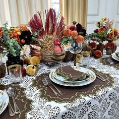 the table is set with plates, silverware and fall flowers in vases on it