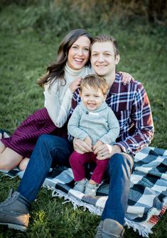 a man and woman sitting on top of a blanket with a baby in their lap