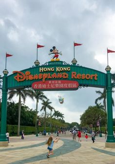 the entrance to hong kong disneyland resort with people walking under it and flags flying in the air