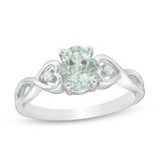 an oval green and white diamond ring with two diamonds on the band, set in 18k white gold