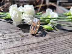 two wedding rings sitting on top of a wooden table next to white flowers and greenery