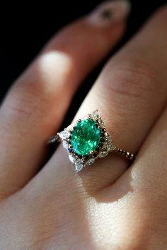 a woman's hand with an emerald and diamond ring on top of her finger