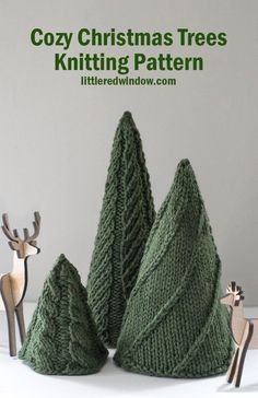 three knitted christmas trees sitting on top of a white table next to deer figurines