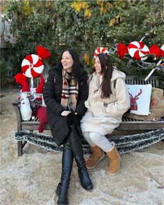 two women are sitting on a bench with candy canes in the trees behind them