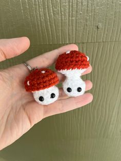 two tiny crocheted mushrooms are sitting on someone's hand, one is wearing a red and white hat