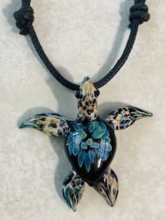 a glass turtle is sitting on a black cord with blue and green flowers in it's shell