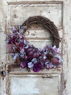 a wreath with purple flowers and pine cones on an old door