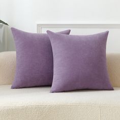 two purple pillows sitting on top of a white couch next to a potted plant