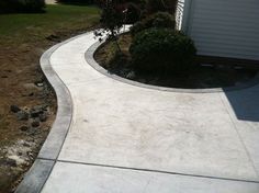 a concrete walkway in front of a house with grass and bushes on the other side