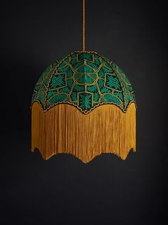 a green and gold hanging light with fringes on the bottom, against a black background