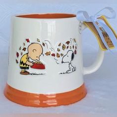 an orange and white coffee mug with a charlie brown cartoon on the side, next to a ribbon