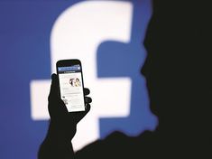 a person holding up a cell phone in front of a screen with the facebook logo