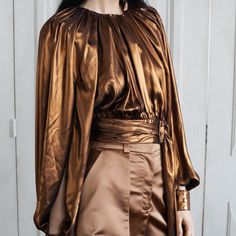 The Rayna Blouse is cut in our novel foil copper gold fabric that fall delicately on the wearer's body. It is a signature Vasiliki Atelier silhouette. Adorned with a ruched belt that hangs onto the side and gold buttons this top features a slit opening along the inside of the full puff sleeves that opens up as you move. The soft shoulder pads add structure to the silhouette.   Pair with our Iconic Mirha Pants in Almond. Dry Clean Only Artisan Fashion, Handloom Fabric, Draped Top, Creative Stuff, Gold Fabric, Clothing Inspiration, Gold Buttons, Independent Designers Fashion, Contemporary Fashion