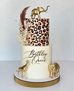 a three tiered cake decorated with gold animal figurines and leopard print on top