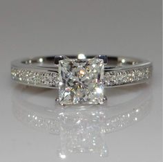 a princess cut diamond ring with pave set diamonds on the band and side stones