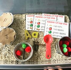 an apple themed activity is displayed in a plastic container with sand and other items on the tray