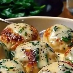 a white bowl filled with ravioli and spinach covered in cheese, on top of a wooden table