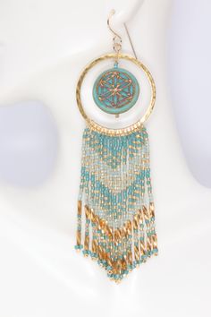 Experience the beauty and spirituality of the mandala with these boho turquoise & gold beaded hoop earrings. Handmade from Czech glass mandala beads, premium delica seed beads, hammered brass hoops, and gold filled ear wires. These fringed beauties will swing and sway their way into your heart with their eye catching mix of hex cut bugle beads, and seed beads in opaque, transparent, and metallic colors. They dangle and dance with the slightest movement. 4.25 inches long 1.25 inches wide Gold Fil Turquoise Artisan Jewelry With Gold Beads, Turquoise Earrings With Gold Beads, Artisan Turquoise Jewelry With Gold Beads, Festival Dangle Jewelry With Gold Beads, Beaded Brass Earrings For Festival, Beaded Hoop Festival Jewelry, Bohemian Blue Wire Wrapped Hoop Earrings, Beaded Hoop Jewelry For Festivals, Bohemian Gold Circle Jewelry