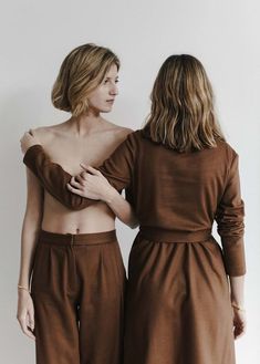 two women standing next to each other wearing brown clothing and one has her back turned towards the camera