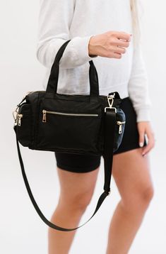 a woman carrying a black handbag with zippers on the front and shoulder straps