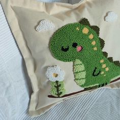 a crocheted pillow with a green dinosaur on it's back and flowers in its mouth