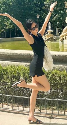 a woman is posing in front of a fountain with her arms up and legs spread out