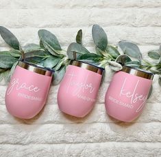 three pink wine glasses sitting on top of a white blanket next to some green leaves