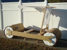 a cart made out of cardboard sitting in front of a white fence