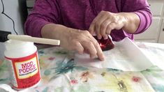 a woman sitting at a table with a jar of glue on top of her hand