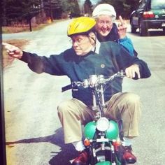 an old man riding on the back of a motorcycle next to a young boy wearing a helmet