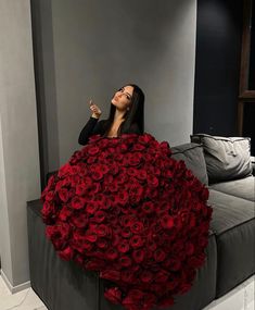 a woman sitting on top of a couch covered in red roses and pointing to the sky