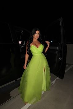 a woman in a green dress standing next to a car at night with her hand on the door