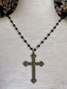 Step back in time with this intricate hand-assembled metal cross rosary-style necklace, featuring a long black beaded chain, and quatrefoil design bronze colored cross pendant. Perfect for tying together a Gothic Medieval, or perhaps Victorian Mourning styled look. This design is part of our handmade collection, making each piece unique. Sizing: One SizeChain Length - 15 inches / 38 CentimetersPendant Length - 3 inches / 7.6 CentimetersTotal Length - 18 inches / 45.5 Centimeters Care Instruction Gothic Black Metal Cross Necklace, Gothic Black Crucifix Cross Necklace, Black Spiritual Jewelry With Antique Finish, Black Beaded Cross-shaped Rosary, Black Beaded Cross Rosary, Ankh Shaped Black Metal Necklace, Beaded Spiritual Cross Pendant Necklace, Black Ankh Necklace In Metal, Black Metal Crucifix Cross Necklace