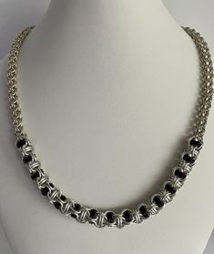 This chainmaille necklace measures 18 inches in length and is a combination of two weaves-open round for the chain and Jacob's Ladder for the focal. Tiny sterling silver rings make up the open round chain which is tubular in form. The focal weave is Jacob's Ladder, a variation of open round that has rings captured within. The medium size sterling rings capture black and frost gray anodized aluminum rings.  The clasp is a 1/4 inch sterling lobster claw.  A truly unique necklace to wear. Silver Jewelry With Box Chain And Round Beads, Silver Necklace With Box Chain And Round Beads, Black Sterling Silver Link Necklace, Metal Necklaces With Rolo Chain, Metal Jewelry With Rolo Chain In Round Shape, Metal Jewelry With Rolo Chain, Elegant Chainmail Chain Link Jewelry, Black Sterling Silver Link Chain Necklace, Metal Rolo Chain Jewelry