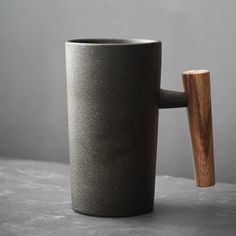 a black cup with a wooden handle on a table next to a gray wall and floor