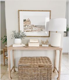 a wicker bench sitting under a painting next to a table with a basket on it