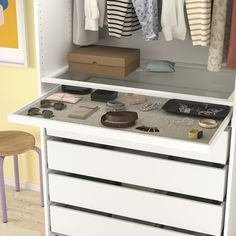 a white dresser with drawers and clothes hanging on the top shelf, next to a stool