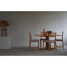 a wooden table with four chairs and a vase on it in front of a white wall