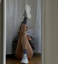 a woman sitting on the floor taking a selfie with her cell phone while wearing tennis shoes