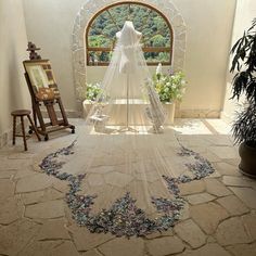 a wedding dress is hanging in the middle of a room with an arched window and potted plants