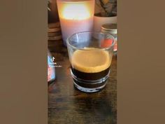 a glass filled with liquid sitting on top of a wooden table next to two candles