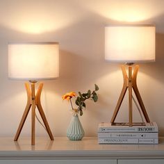 two lamps sitting on top of a table next to books and a vase with flowers