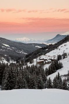 the sun is setting in the mountains with snow on the ground and trees around it