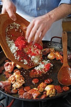 a man cooking food in a pan on the stove with a wooden spoon and spatula