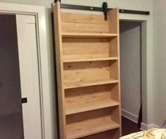 a bed with a wooden book shelf next to a white door in a room that has gray walls and wood flooring