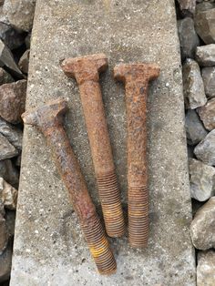 two rusty nails laying next to each other on top of a stone slab with rocks in the background